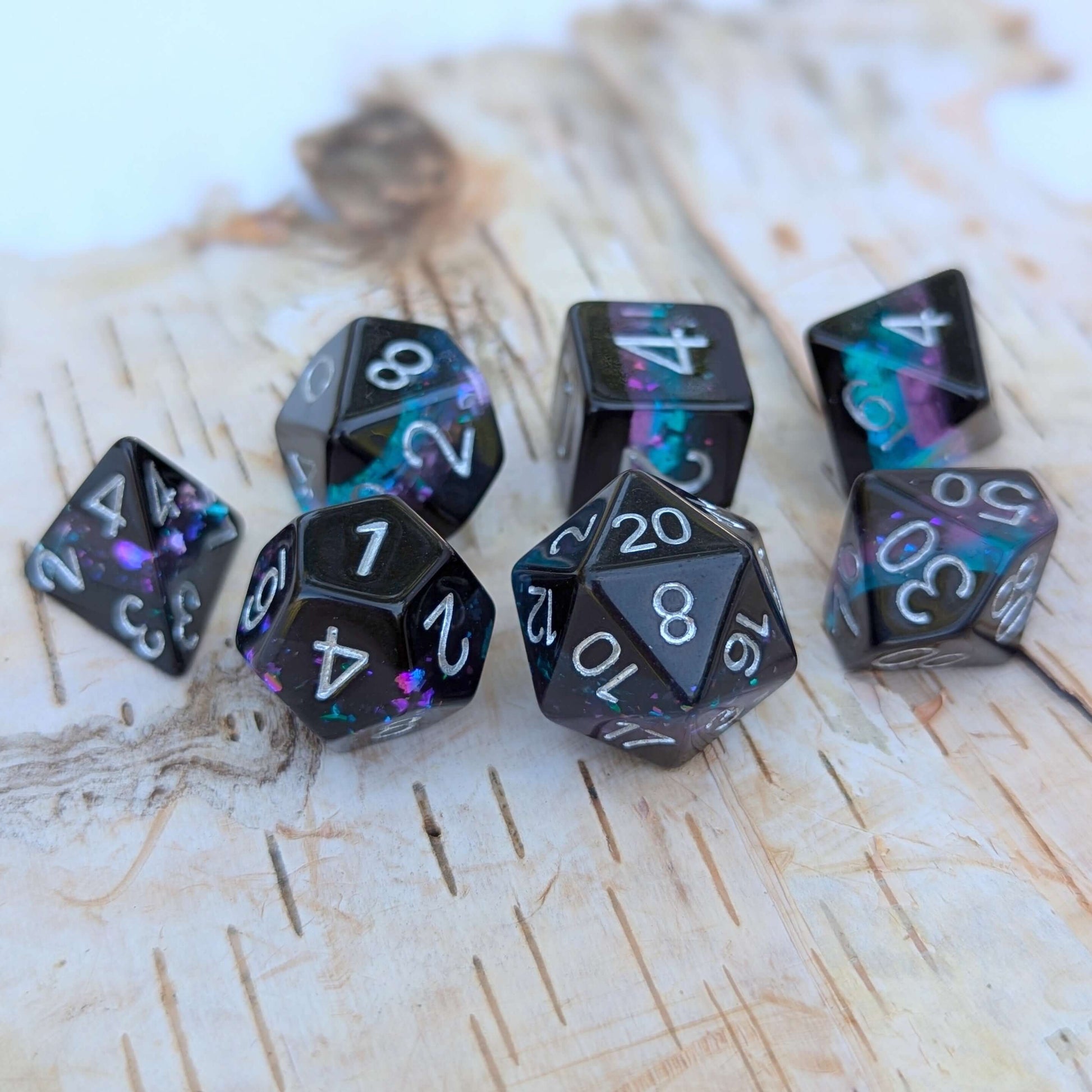 Midnight Nebula dice set on wooden background, featuring round-edge dice with black, blue, and purple glittery layers.