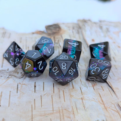 Midnight Nebula round-edge dice set with black, blue, and purple layers, featuring glitter flakes, on a textured, light-colored surface.