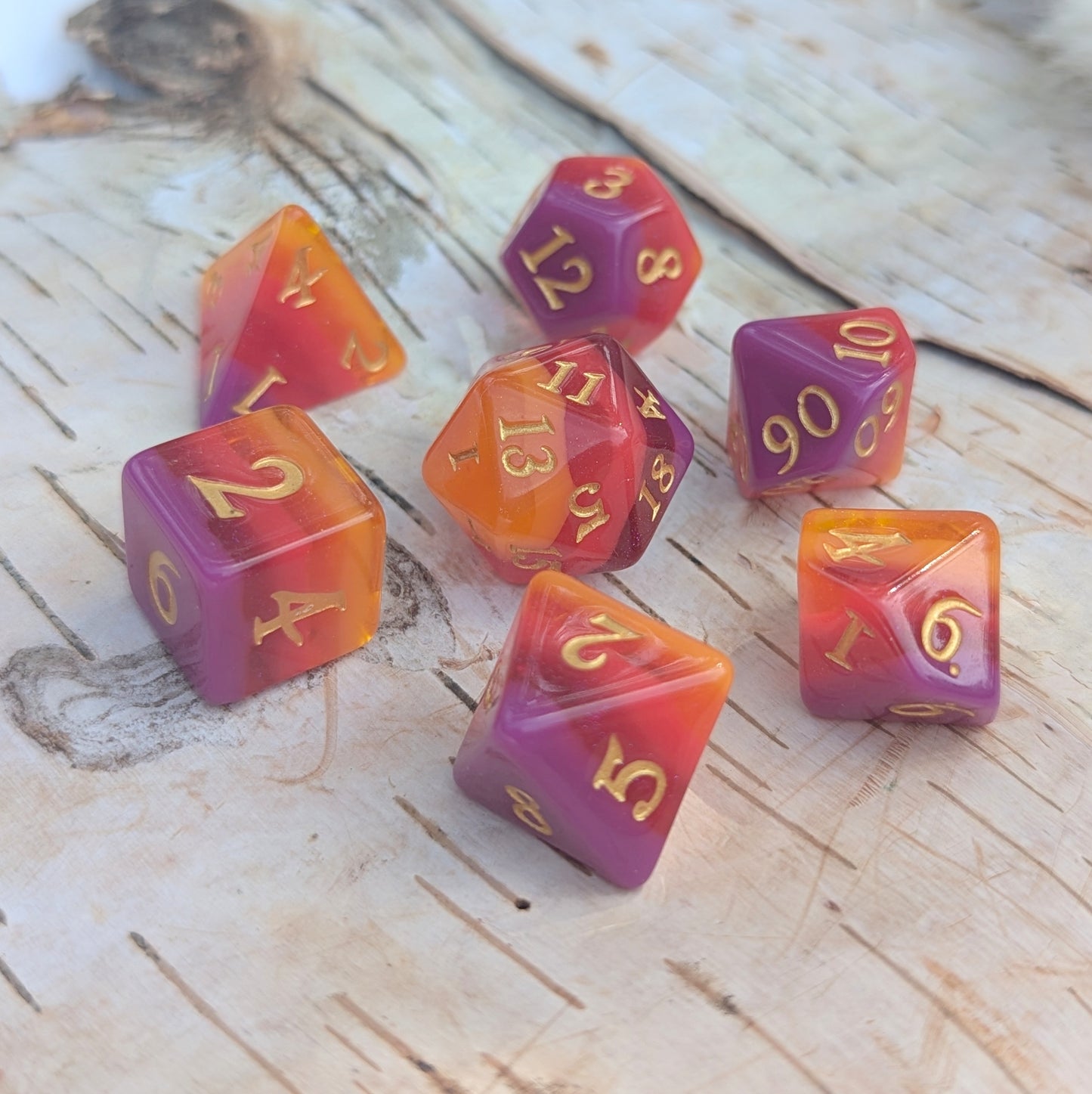 Emberstorm Dice Set featuring vibrant dice with a fiery ombre effect in purple, red, and orange with shimmering gold numbers.