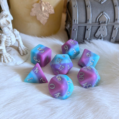 Twilight Serenity Dice Set in blues and purples with a matte finish, displayed near a rustic chest and decorative candle on a soft surface.