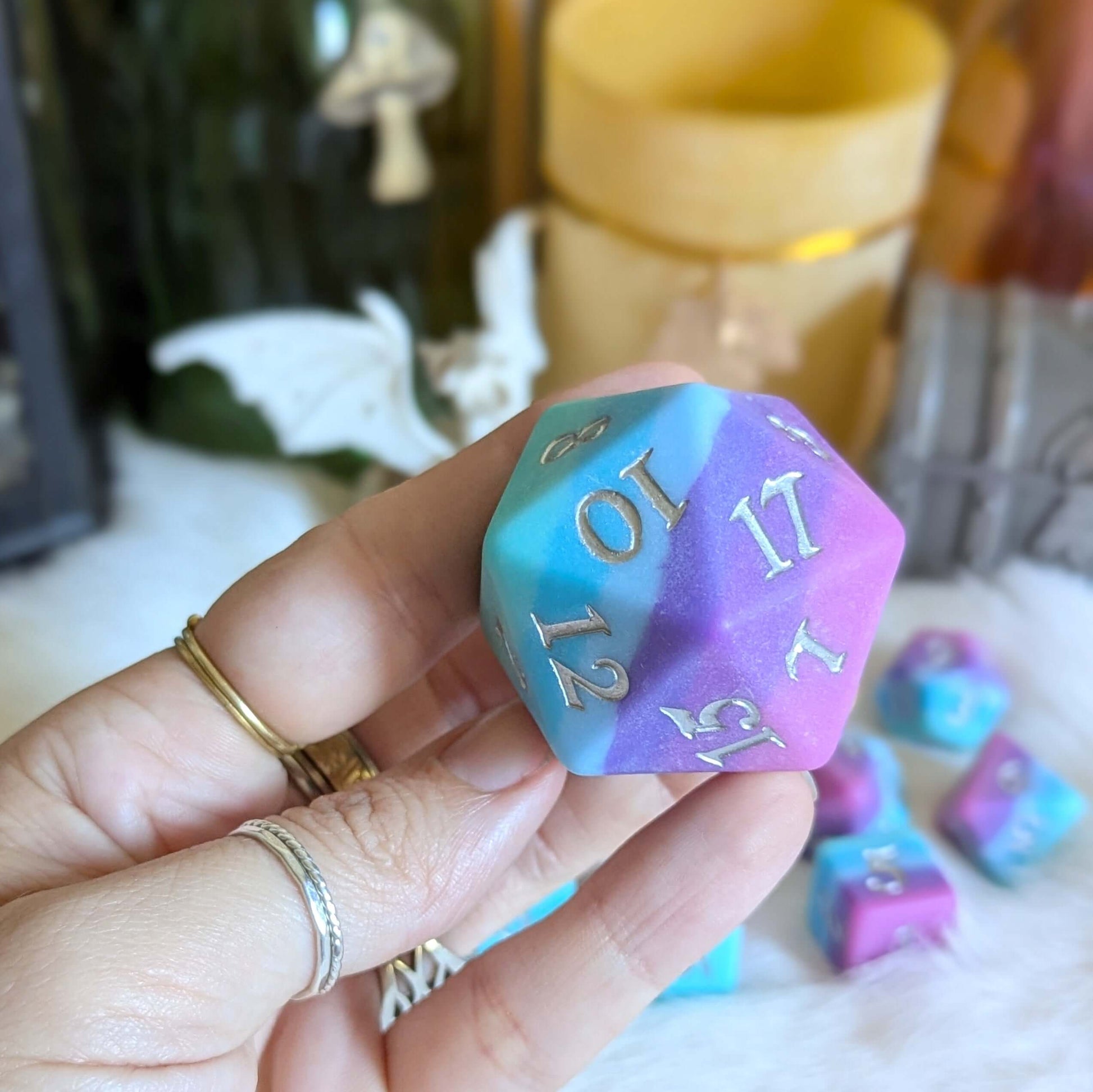 Hand holding Twilight Serenity Large D20 die with ombre colors from teal to purple, silver numbers, and matte finish.