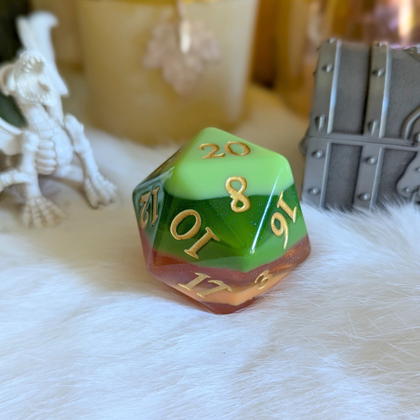 Multicolored D20 die with gold numbers on a white fur surface, surrounded by fantasy props, including a dragon figure and treasure chest.