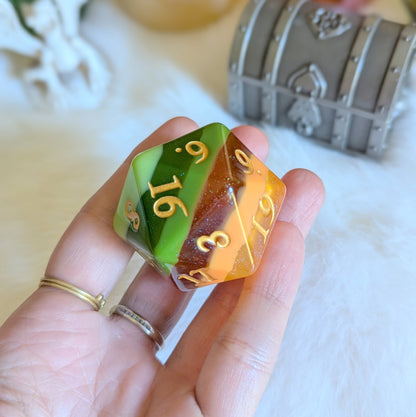 Hand holding a colorful D20 die with green, gold, and orange marbling and gold numbers, against a fantasy-themed backdrop.