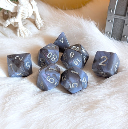 Moonlit Mirage Dice Set with round edges and grey-blue marbled swirls, highlighted by deep black and pink glitter accents.