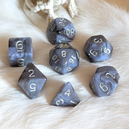 Moonlit Mirage Dice Set with grey-blue swirls and black accents on a white fur background.