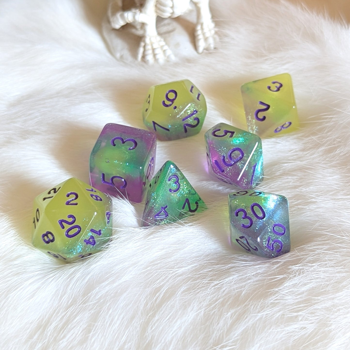 Dreamlight Grove dice set with green-yellow, teal, and purple swirls, featuring glow-in-the-dark and glitter effects on a white fur background.