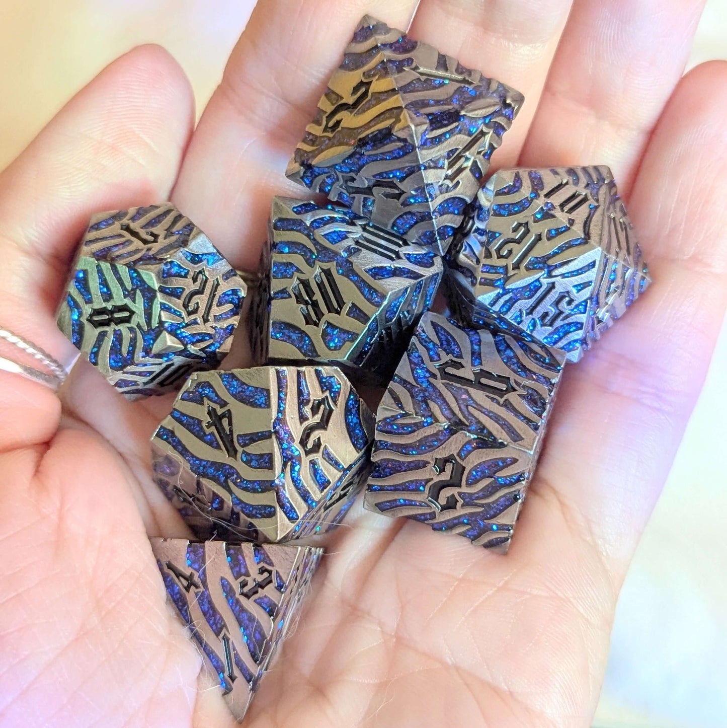 Hand holding Silverfang Metal Dice Set with claw scratch designs and blue glitter, resembling ocean waves.