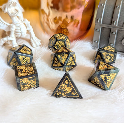 Kambaba Jasper Rose Gemstone Dice Set with gold-engraved roses on a fluffy white surface, dragon and treasure chest in background.