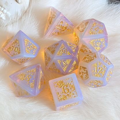 Pink opalite gemstone dice set with gold rose vine engravings on a soft white background.