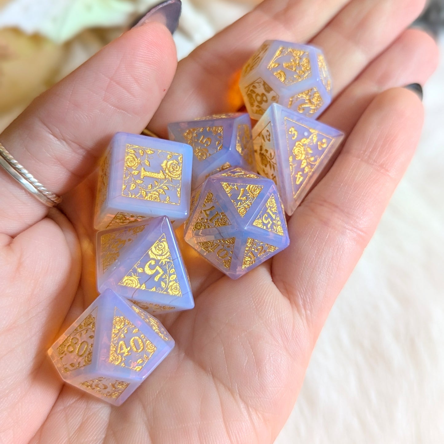 Hand holding Pink Opalite Rose Vine Gemstone Dice Set with gold engravings and ethereal glow.