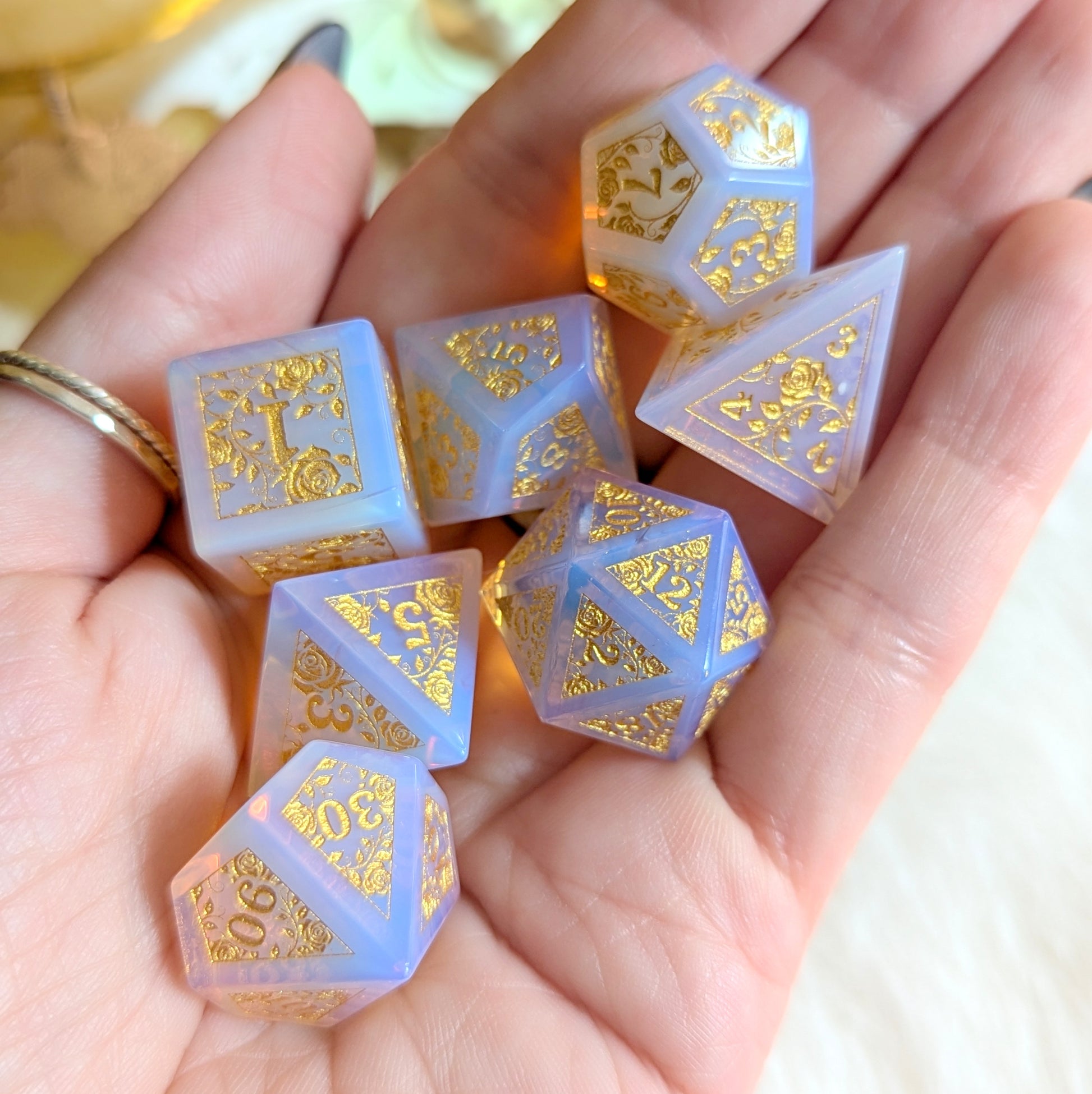 Pink Opalite Rose Vine Gemstone Dice Set with gold engravings in a hand, showcasing its magical glow and elegance