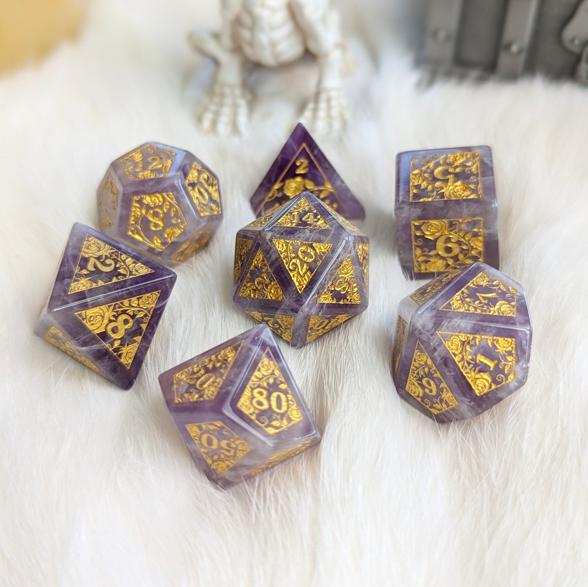 Amethyst Rose Vine Gemstone Dice Set with gold engravings on marbled purple and white background, displayed on soft white fabric.