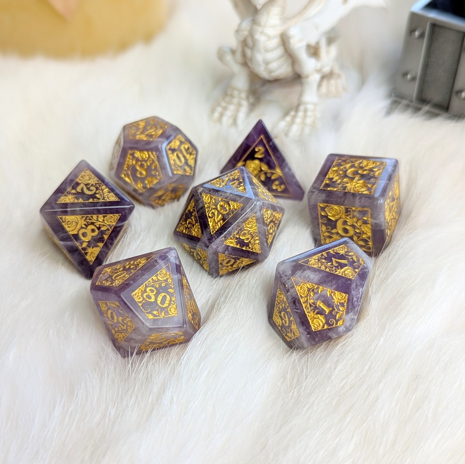 Amethyst Rose Vine Gemstone Dice Set with gold engravings on fluffy white surface.