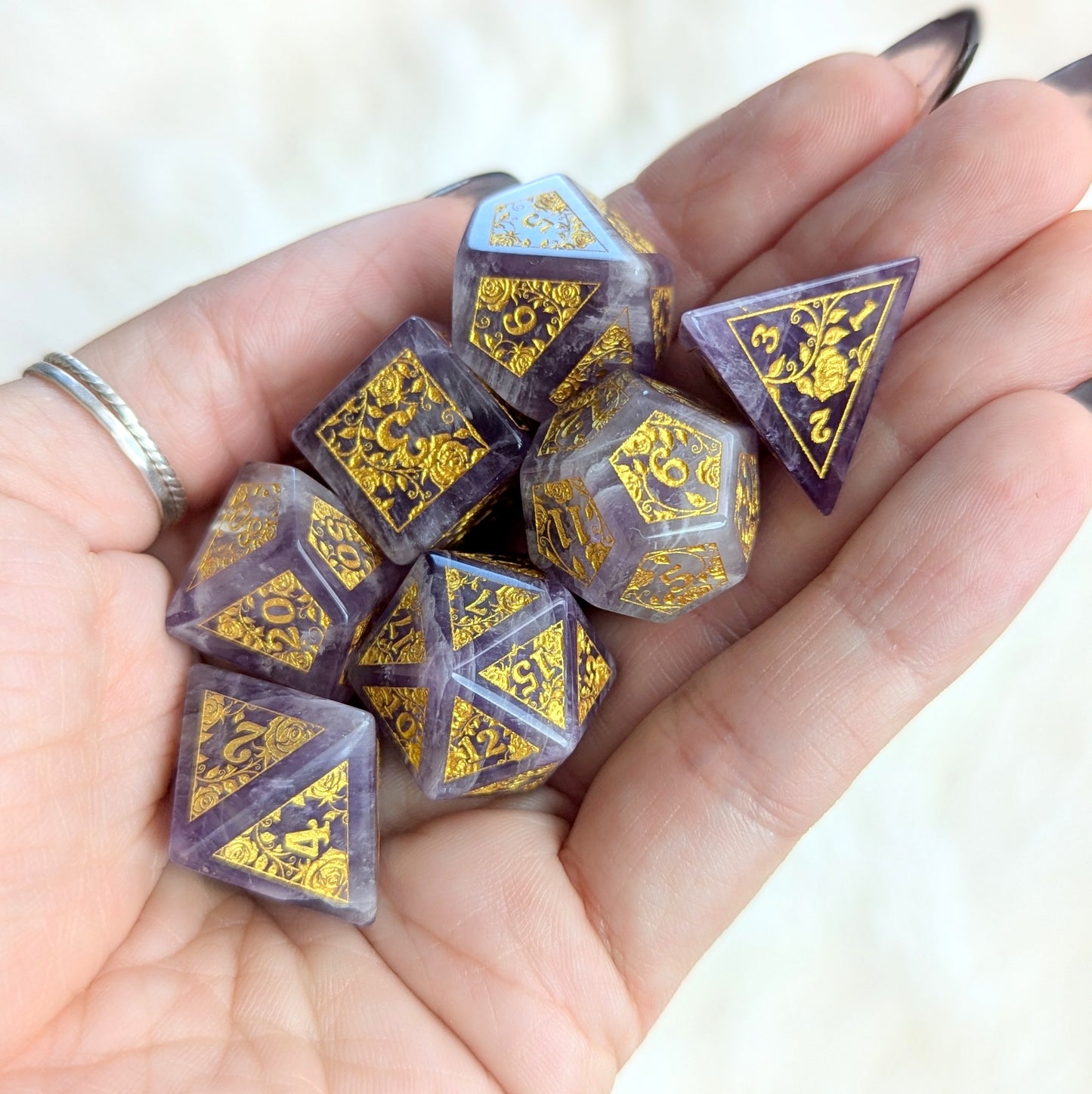 Hand holding Amethyst Rose Vine Gemstone Dice Set with purple and white marbled design and gold vine engravings.