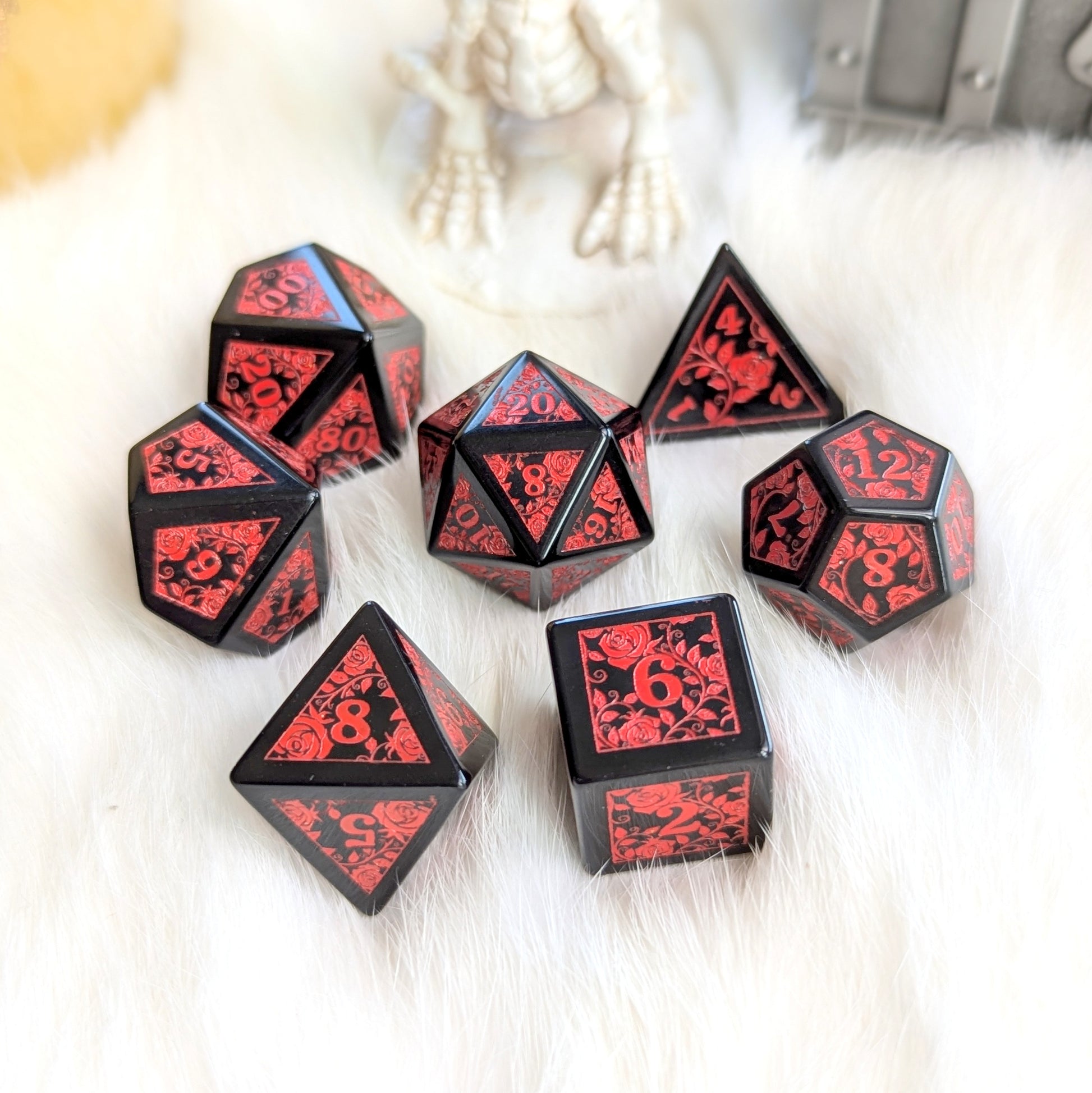 Obsidian Rose Vine Gemstone Dice Set with red floral engravings on black obsidian dice, showcasing elegance and intensity against white fur.