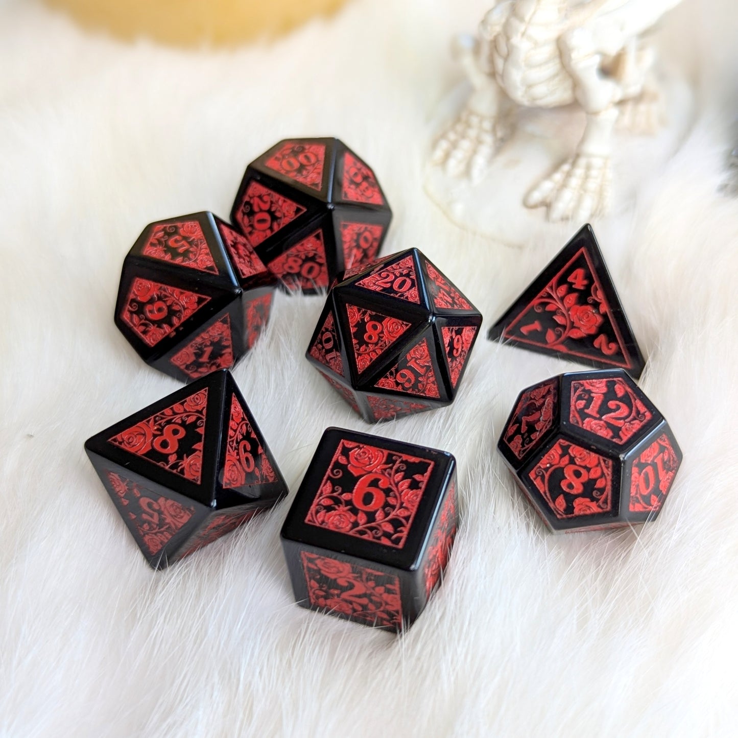 Obsidian Rose Vine Gemstone Dice Set with red rose engravings on black obsidian, displayed on a soft white surface.