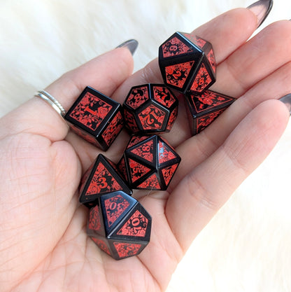 Hand holding Obsidian Rose Vine gemstone dice set with red rose vine engravings on polished black surfaces, evoking elegance and intensity.