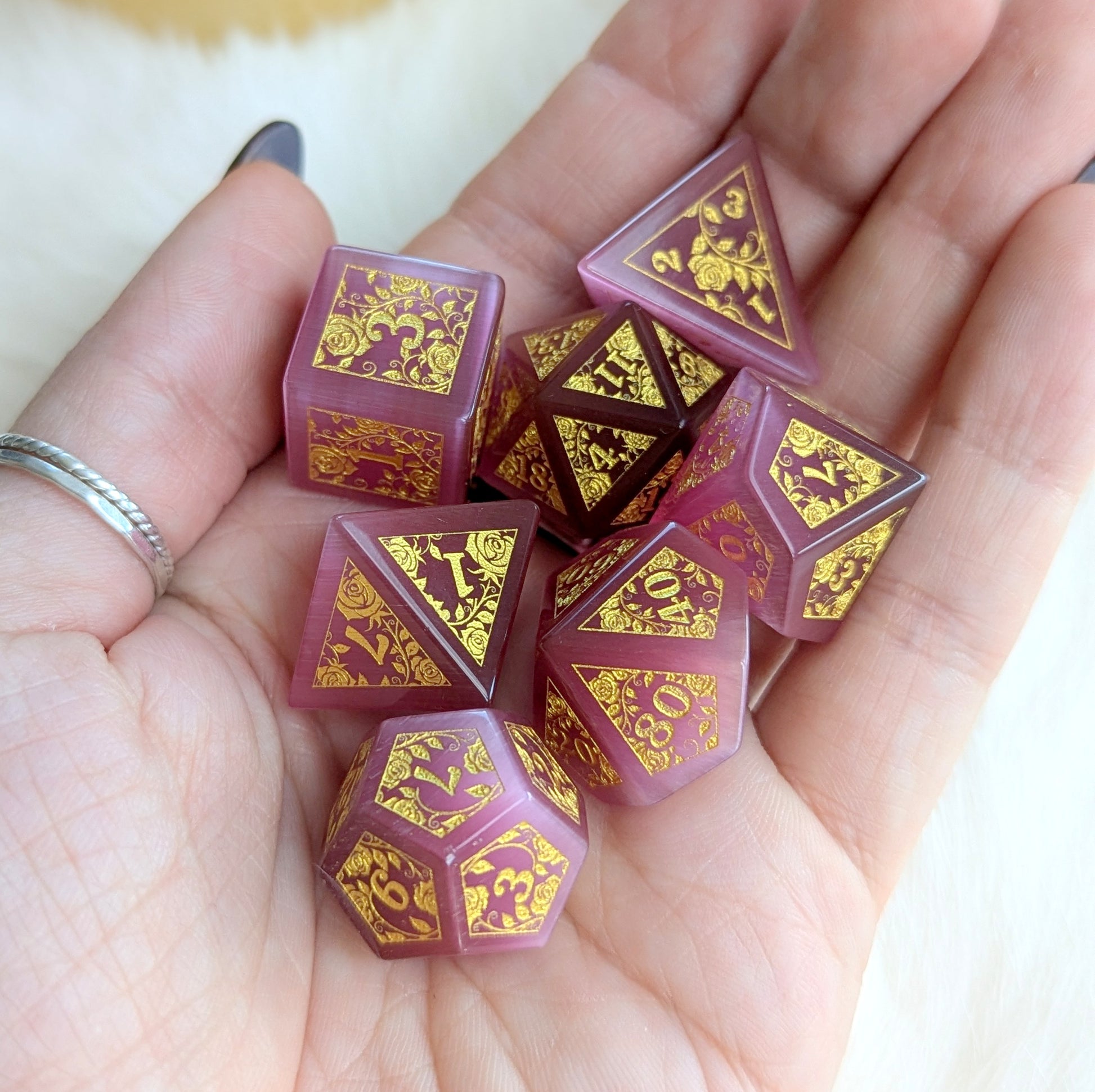 Hand holding Rose Cat’s Eye Rose Vine Glass Dice Set with gold-engraved designs and deep rose pink shimmer.