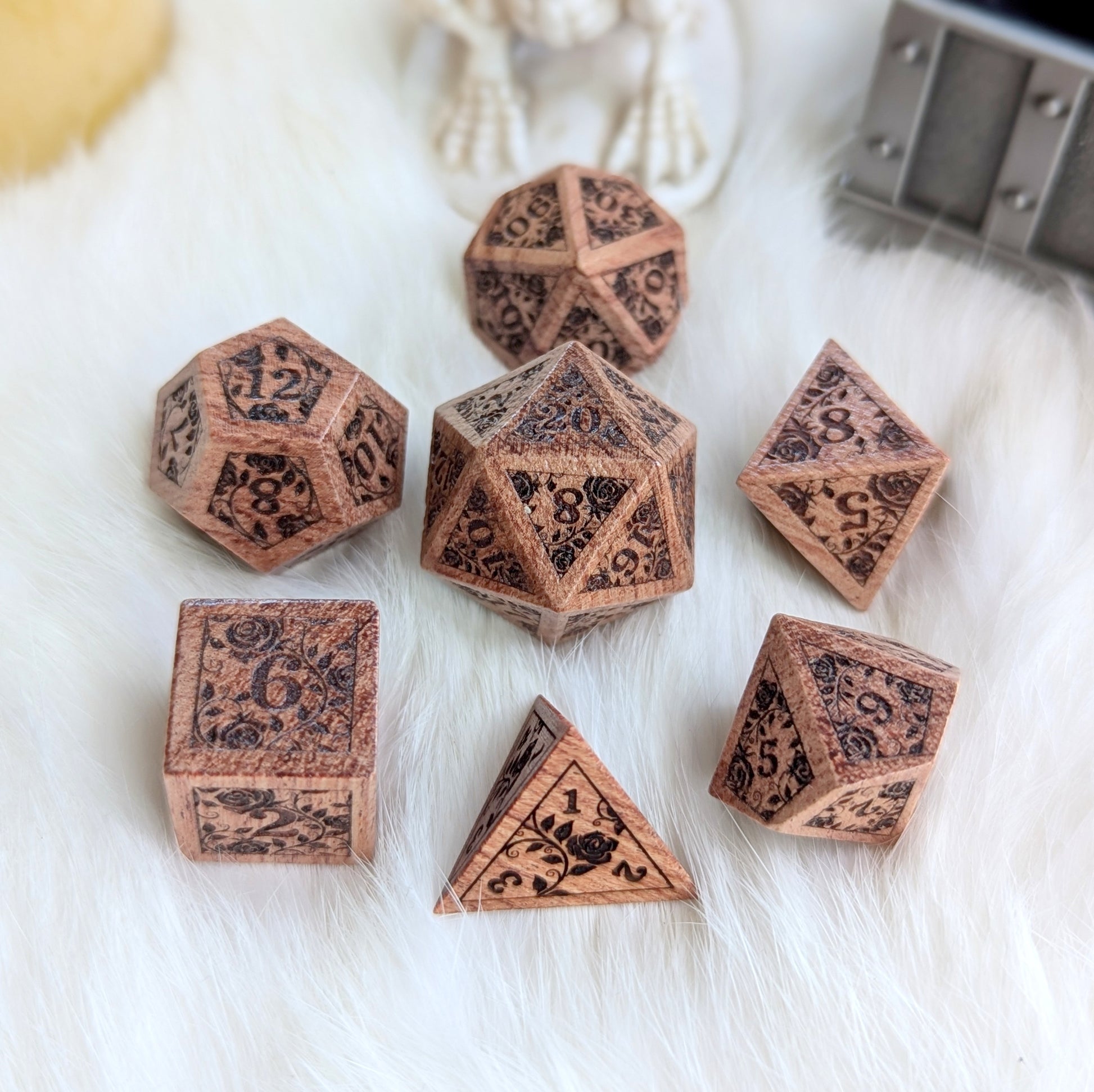 Rosewood dice set with engraved rose vine design on white fur background.