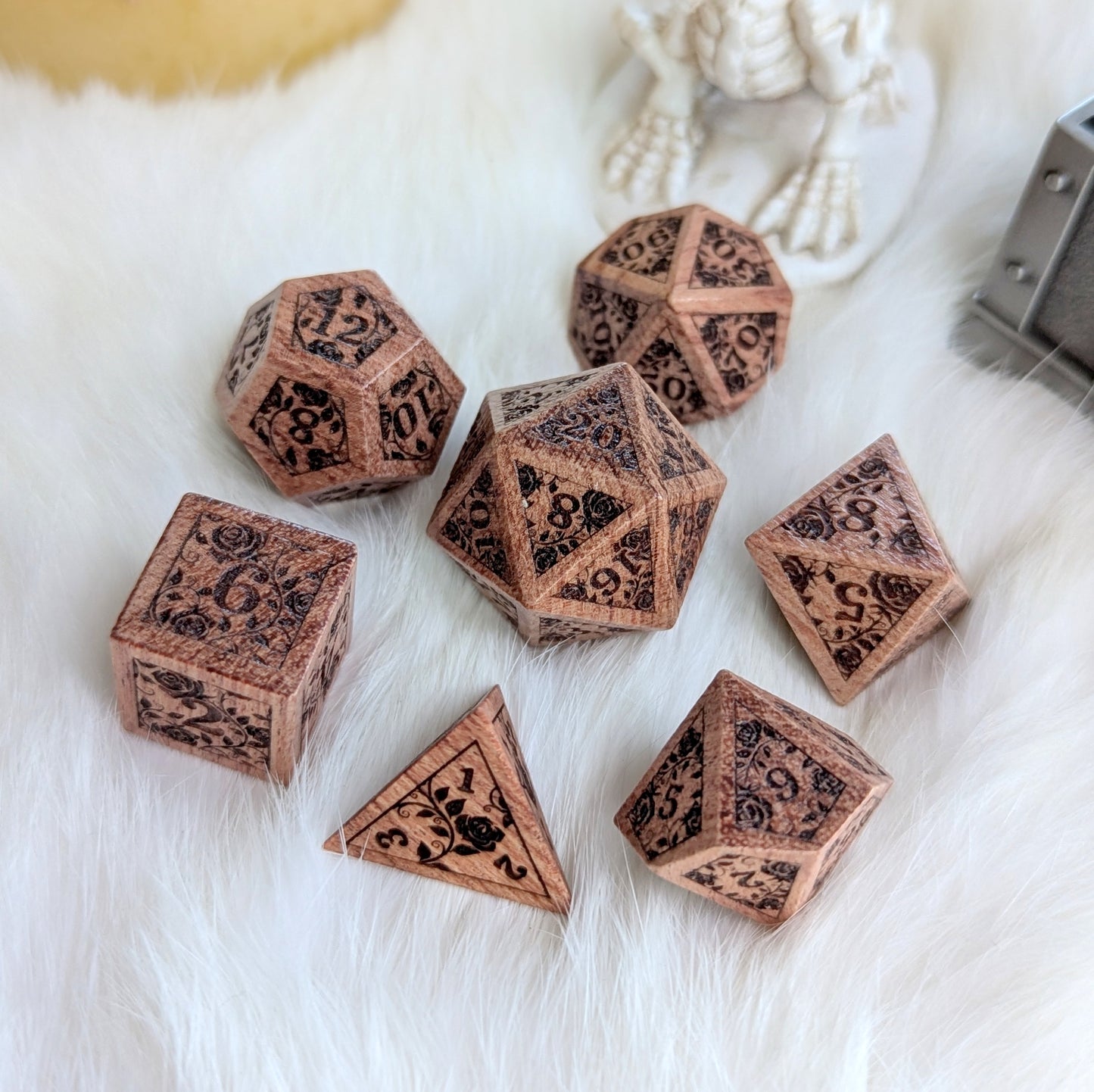 Rosewood dice set engraved with rose vine designs on a soft white background.