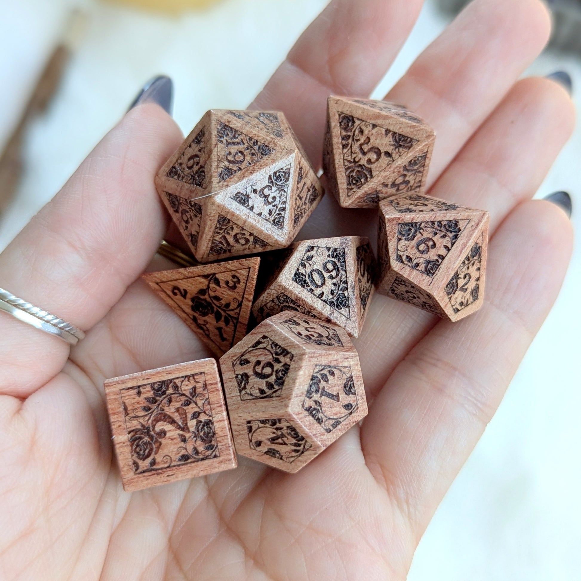 Hand holding Rosewood Rose Vine Engraved Dice Set showcasing intricate floral designs and rich wood texture.