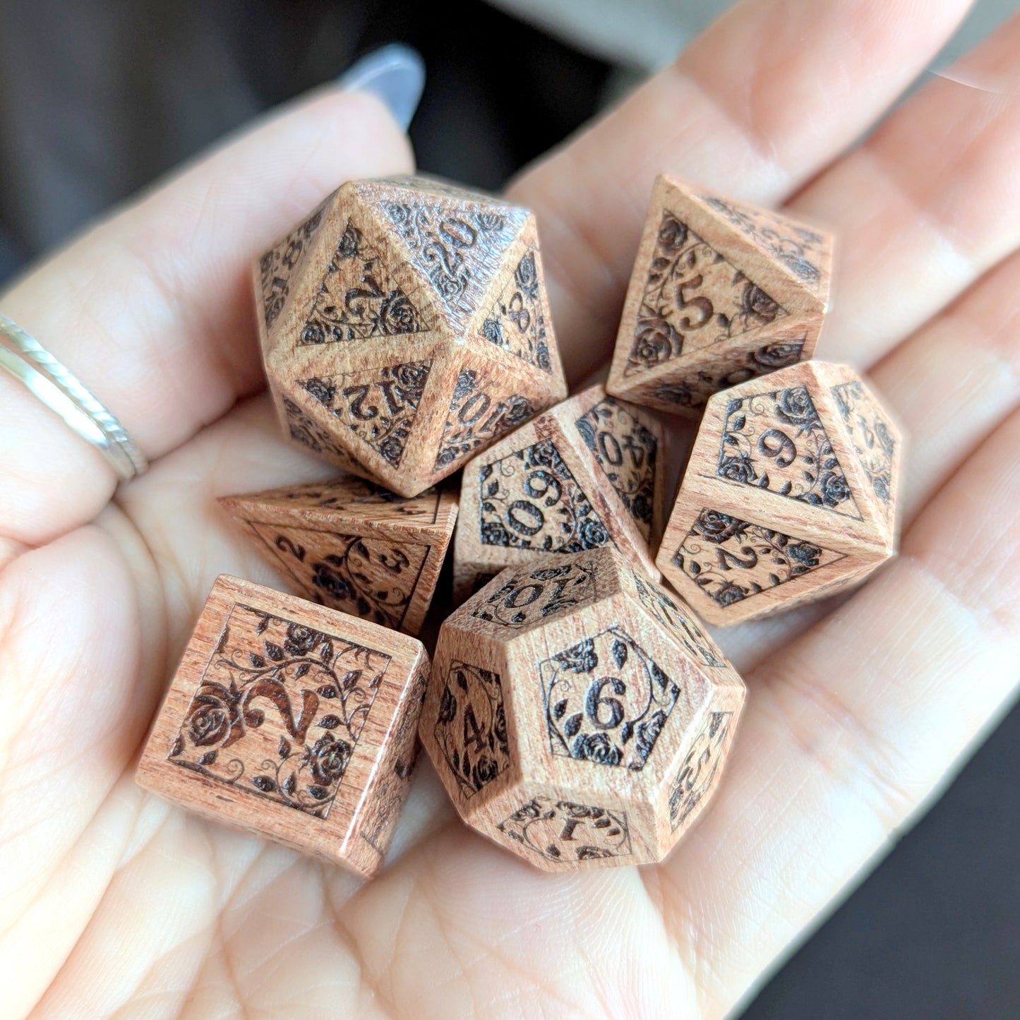 Hand holding Rosewood Rose Vine Engraved Dice Set with intricate floral designs.