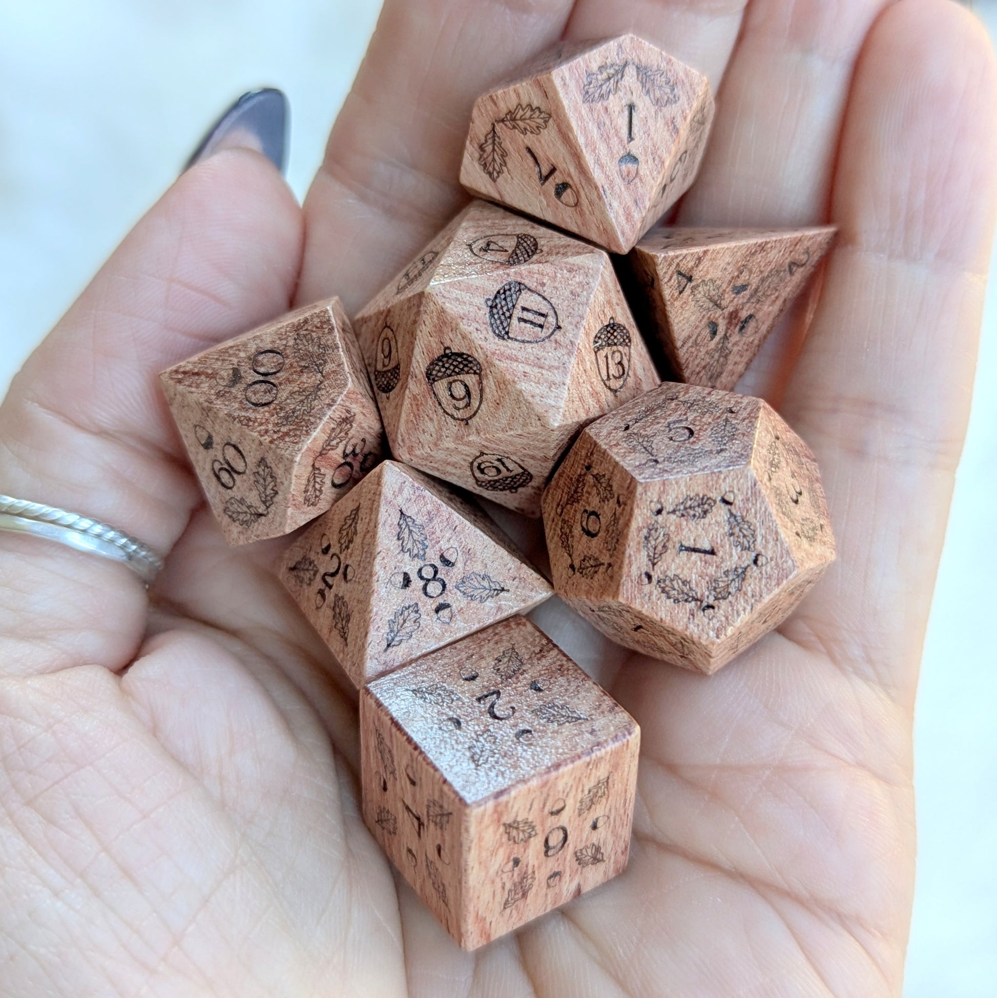 Hand holding Oak Grove Engraved Rosewood Dice Set with acorn and oak leaf engravings.