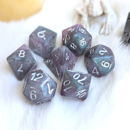 Shadow Veil Dice Set with shimmer grey, purple, and black hues, featuring round edges and silver numbers, placed on soft fabric.