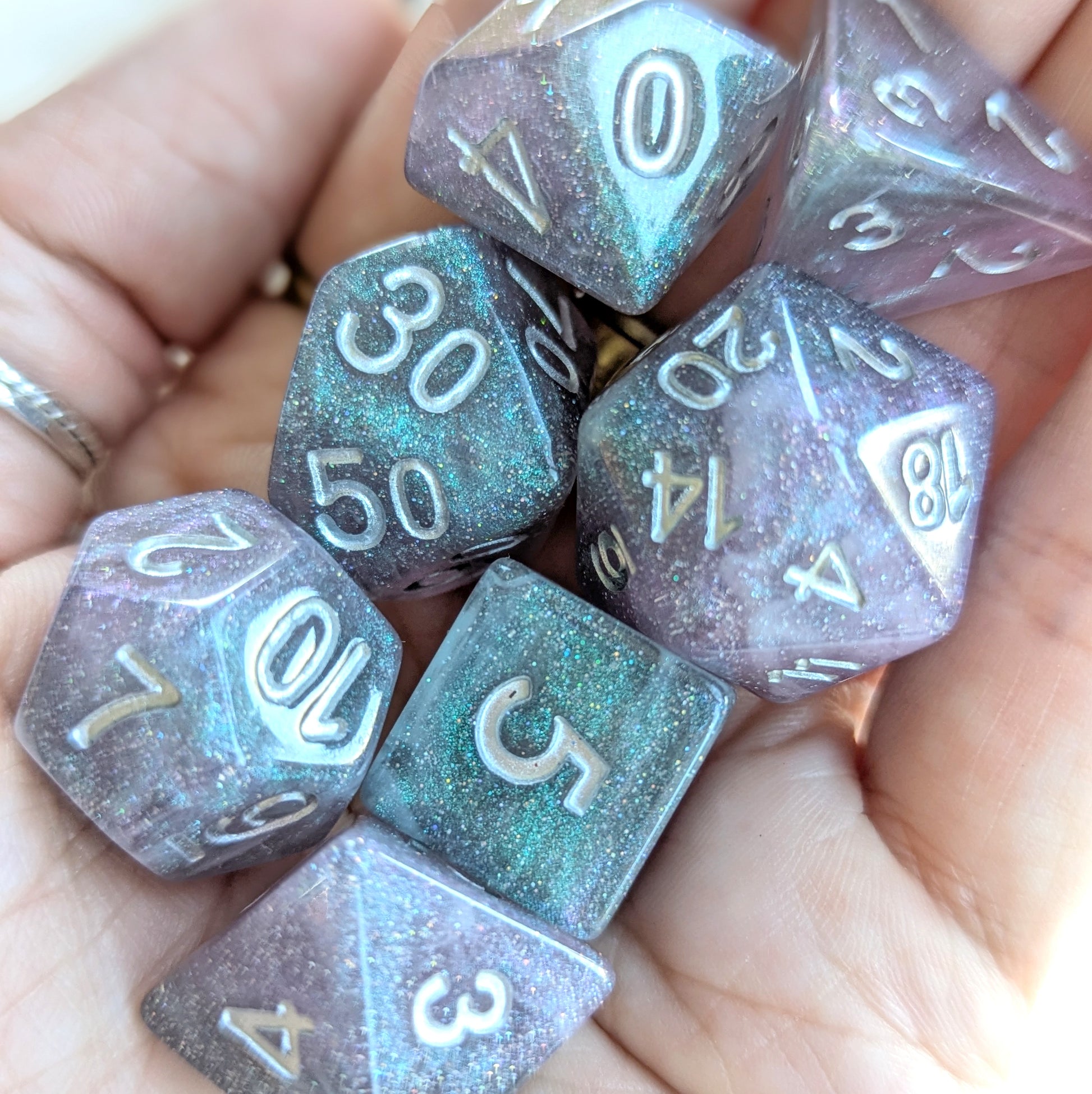 Shadow Veil round-edge resin dice set with shimmering grey, purple, and black hues, held in hand, ideal for tabletop gaming.