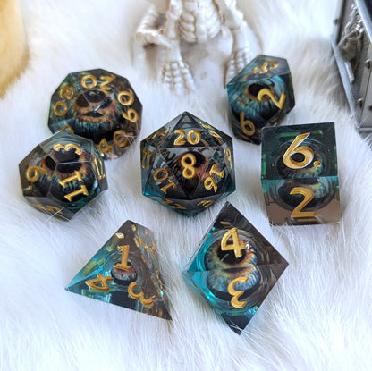 Watcher’s Gaze Liquid Core Dice Set with sharp edges, featuring a mystical eye design in deep blue and black resin with gold numbers.