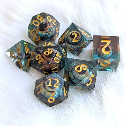 Watcher’s Gaze Liquid Core Dice Set with sharp edges, featuring a mystical eye in deep blue and black resin with gold numbers.