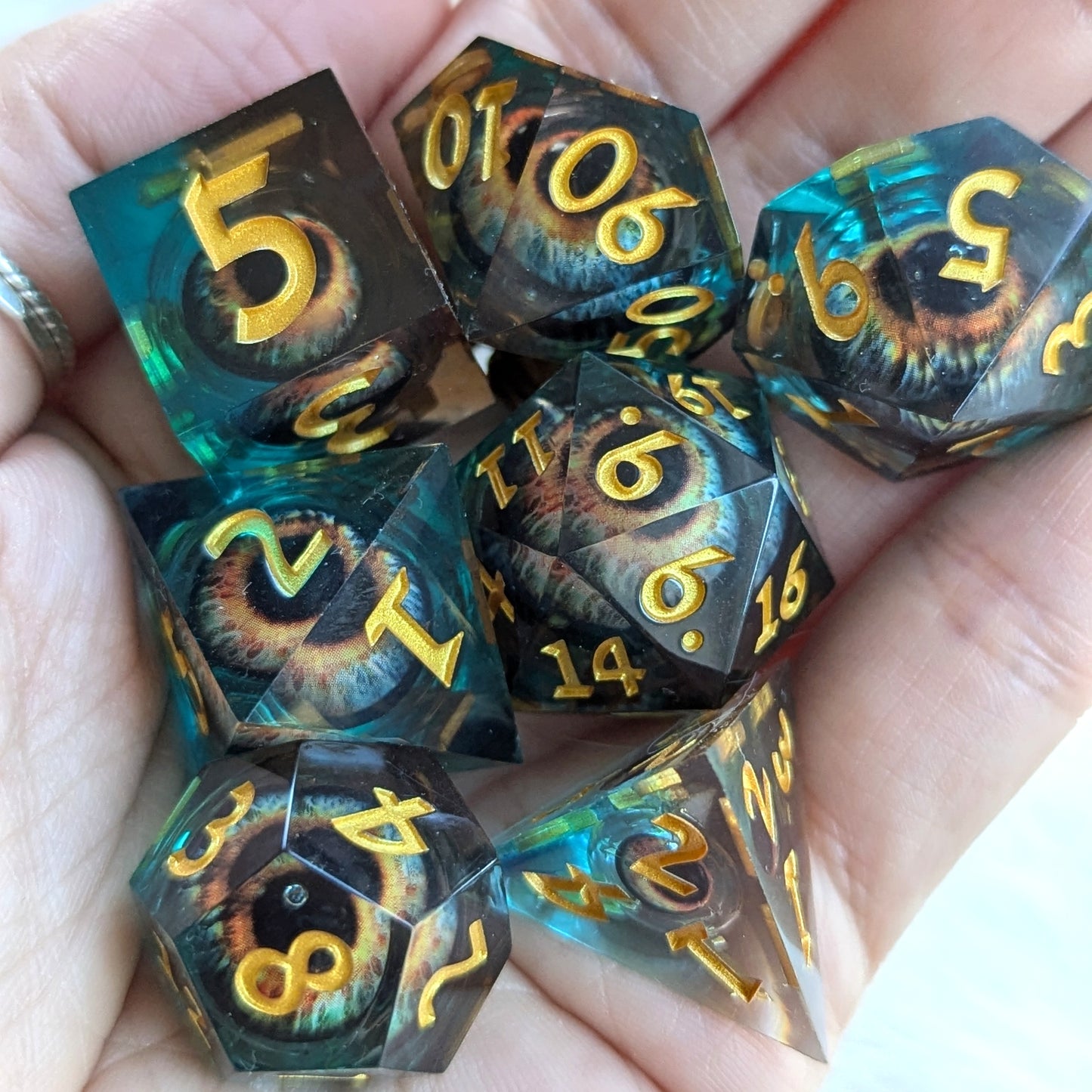 Watcher's Gaze Liquid Core Sharp Edge Dice Set with eye design in blue resin held in hand