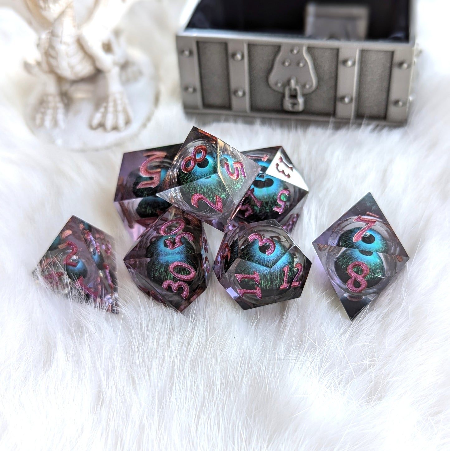 Mystic Eye Dice Set with purple resin and floating blue-green eye, displayed on white fur near a treasure chest.