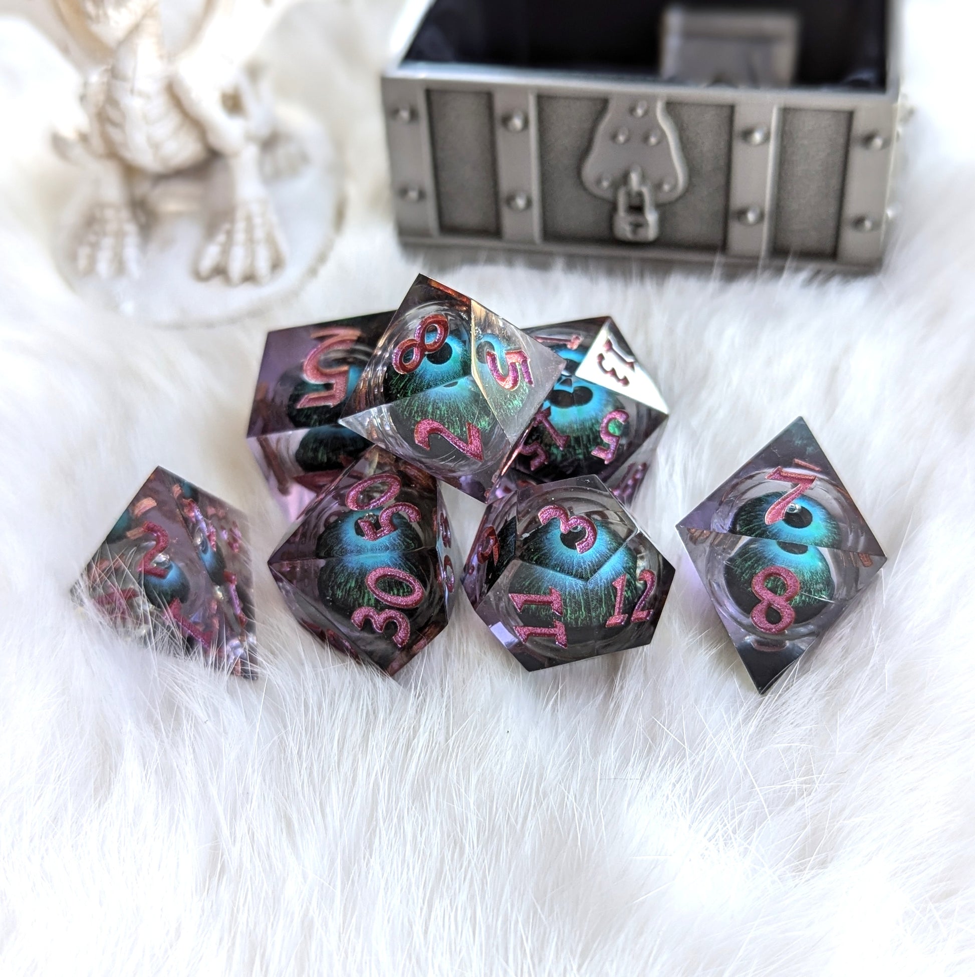 Mystic Eye Dice Set with purple resin and floating blue-green eye, displayed on white fur near a treasure chest.