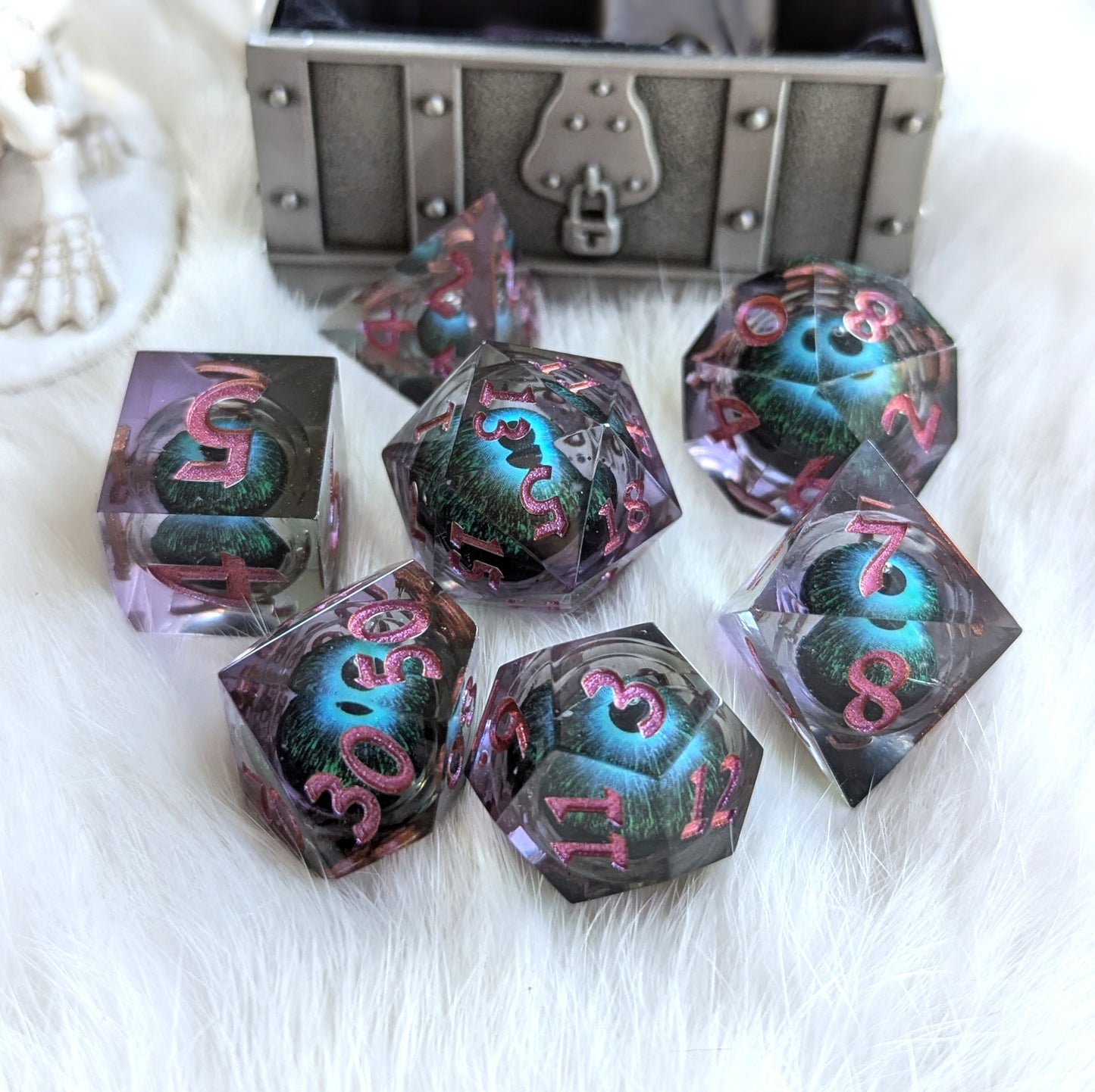 Mystic Eye Liquid Core Dice Set with blue-green eye design in sharp-edge purple resin, displayed on a fluffy white surface.