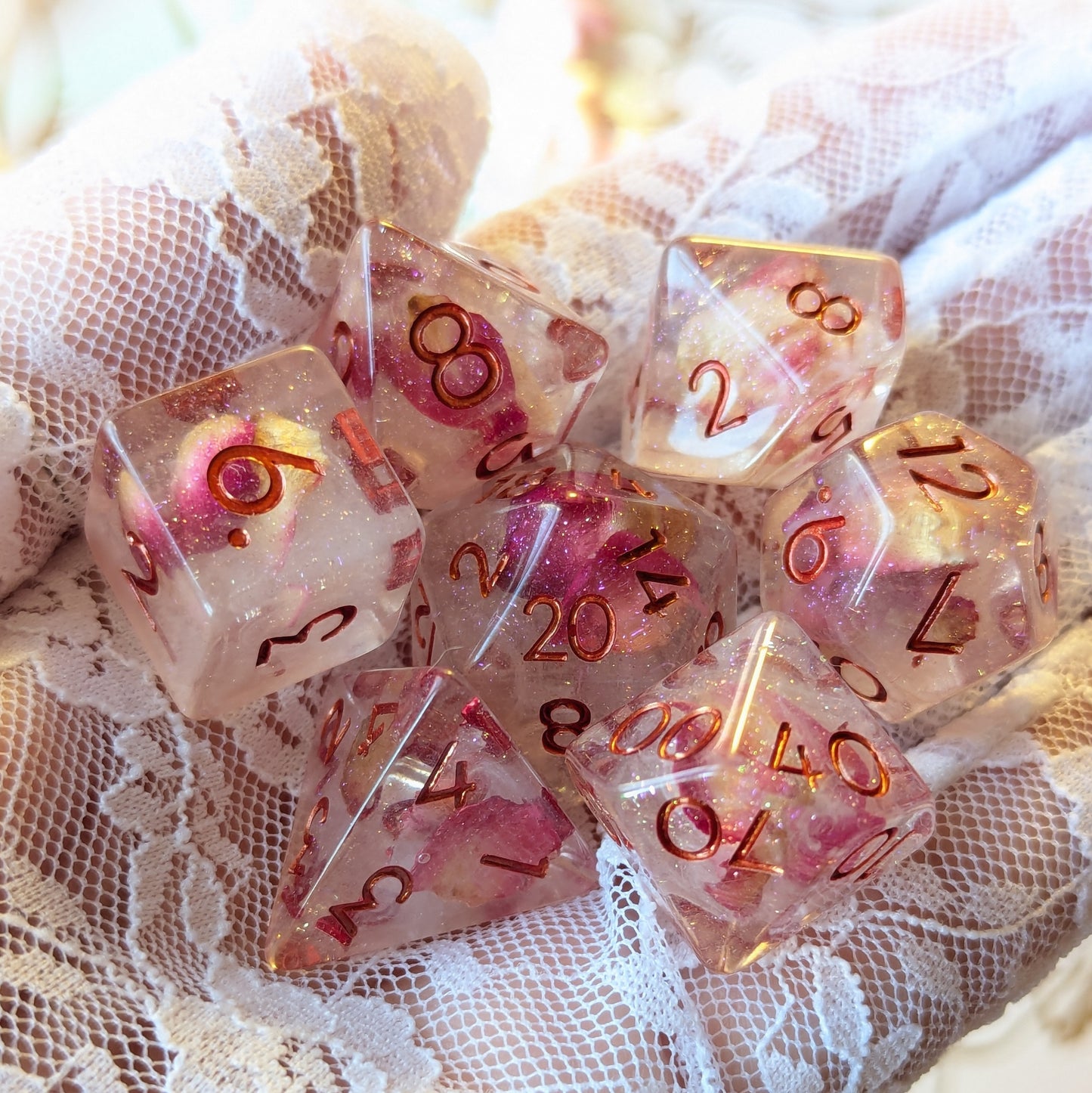 Eternal Rose Dice Set showcasing seven resin dice with pink petals and glitter on a lace background.