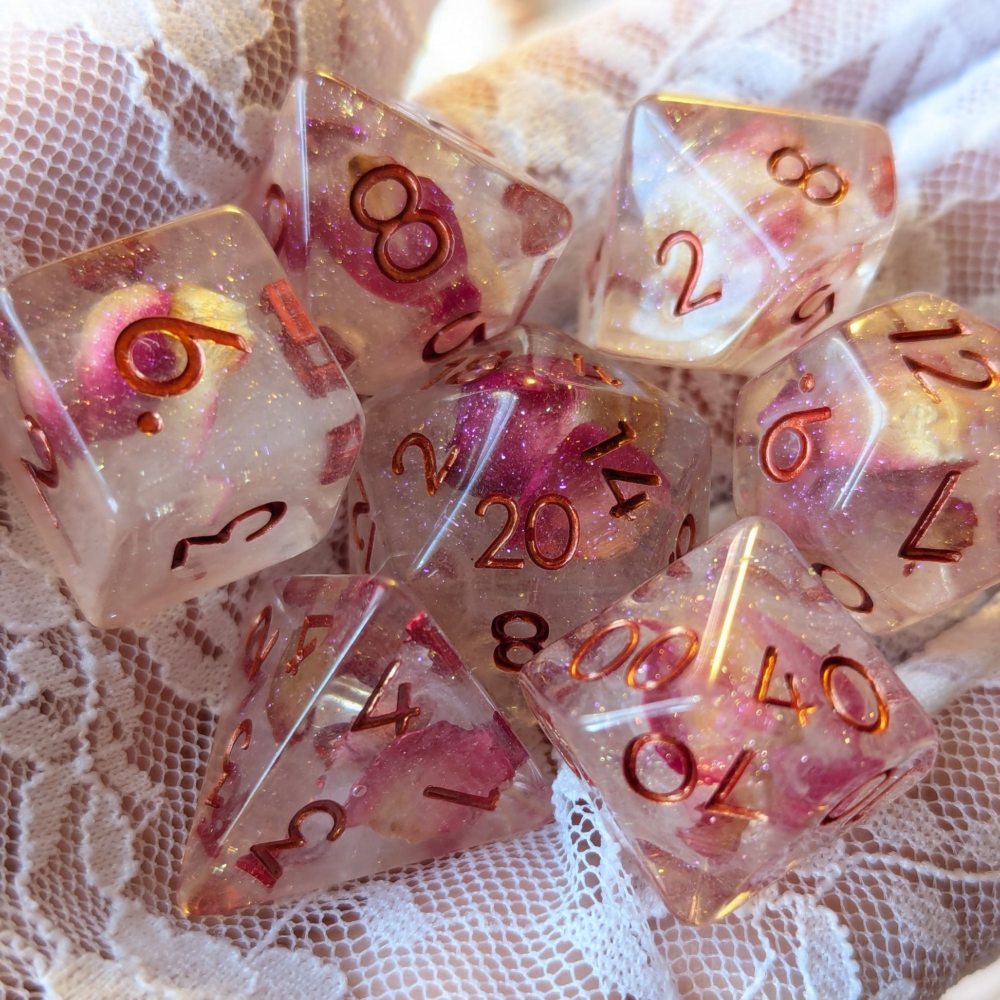 Eternal Rose Dice Set featuring pink rose petals in resin with metallic red numbers on a lace background.