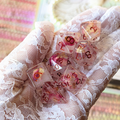 Eternal Rose Dice Set held in a lace-gloved hand, showcasing pink rose petals and shimmering glitter in resin.