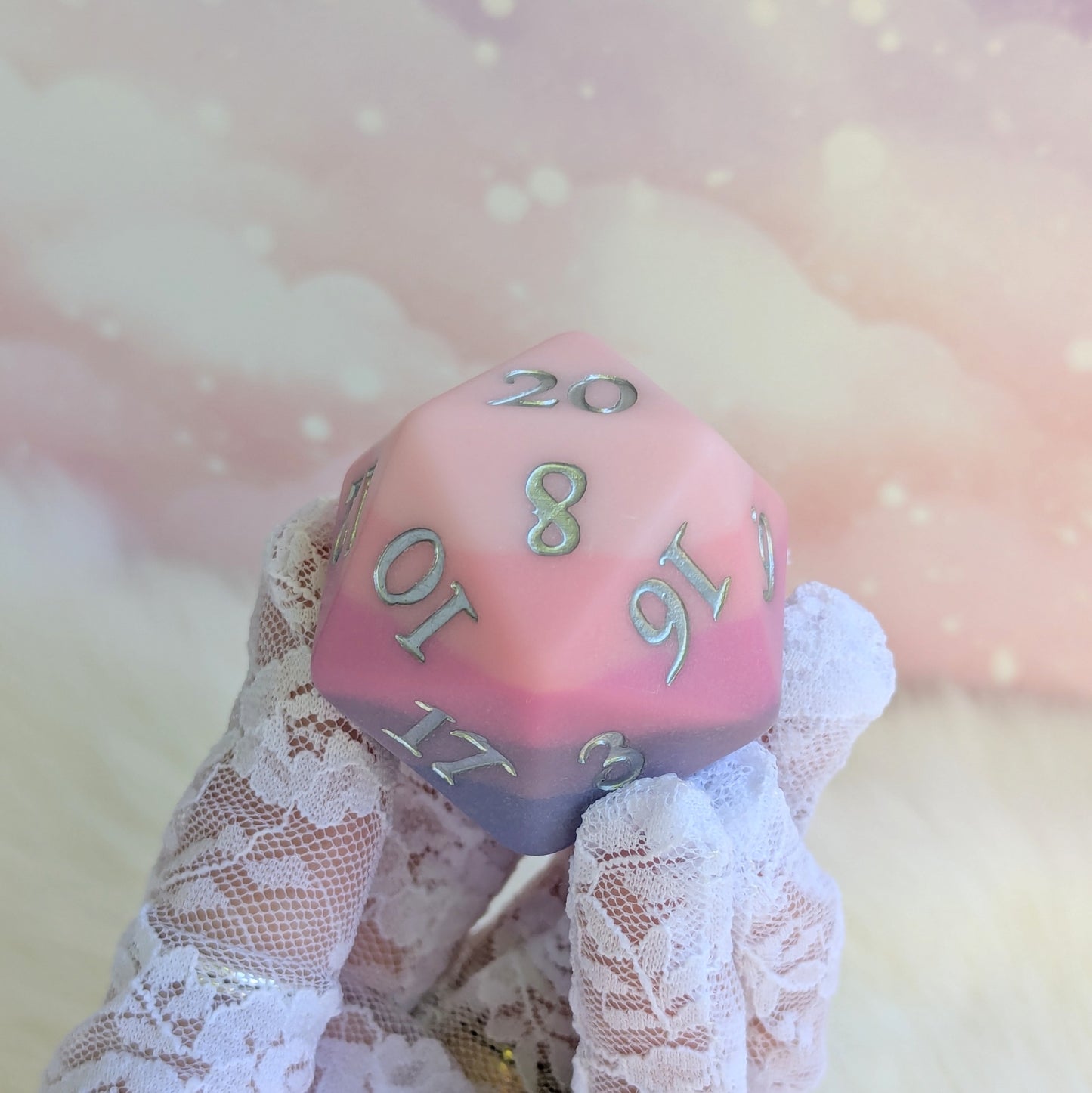 Dreamweaver Large D20 die in pink and lavender hues held in a gloved hand, showcasing its unique matte finish.