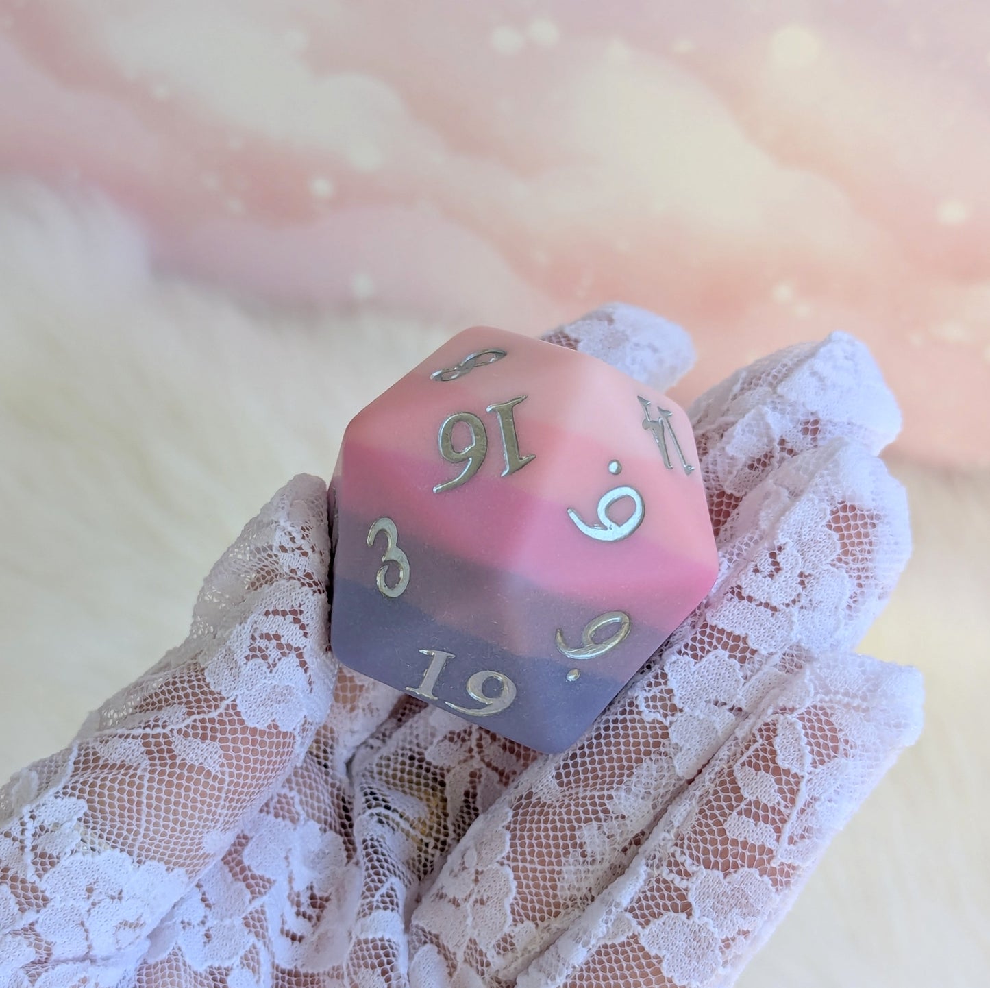 Dreamweaver Oversized D20 die in matte ombre design held gently, featuring shades of pink and lavender with silver numbers.