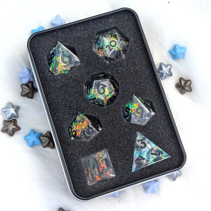 A set of holographic polyhedral dice displayed inside a black foam-lined metal tin, surrounded by scattered star-shaped decorative pieces on a white faux-fur surface.
