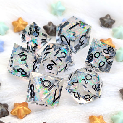 A set of holographic polyhedral dice with black printed numbers, scattered on a white faux fur surface with small pastel and metallic star-shaped props.