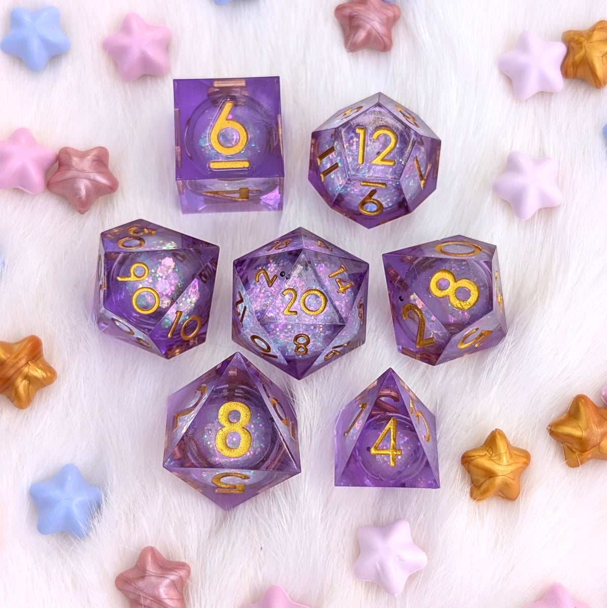 A set of translucent purple polyhedral gaming dice with gold numbers, arranged on a white faux fur background with scattered pastel and metallic star-shaped decorative pieces.