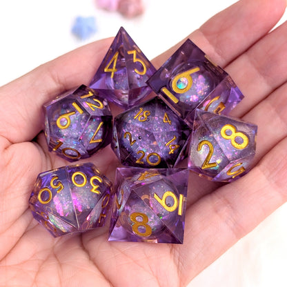 A set of seven purple glitter polyhedral dice with gold numbers, held in a person's hand against a white background.
