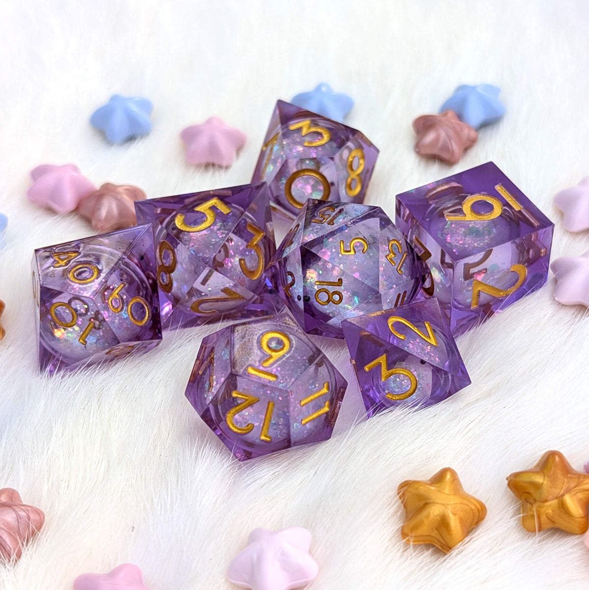 A set of translucent purple polyhedral gaming dice with gold numbering, arranged on a white faux fur surface with pastel star-shaped props.