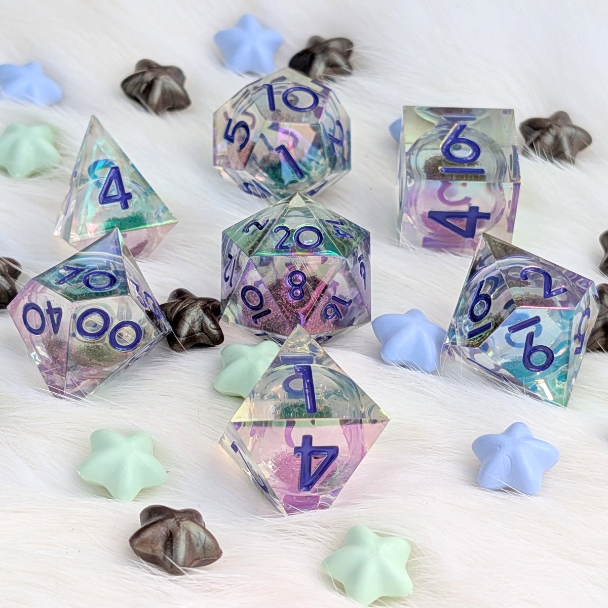 A set of holographic polyhedral dice with blue printed numbers, arranged on a white faux fur surface with decorative pastel star-shaped and flower-shaped props.