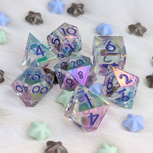 A set of holographic polyhedral gaming dice with blue printed numbers, arranged on a white faux fur surface with pastel star-shaped and shell-shaped decorative props.