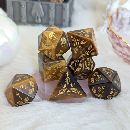 Acorn and Oak Tiger Eye Dice Set with engraved acorn and leaf designs, displayed on a furry surface.