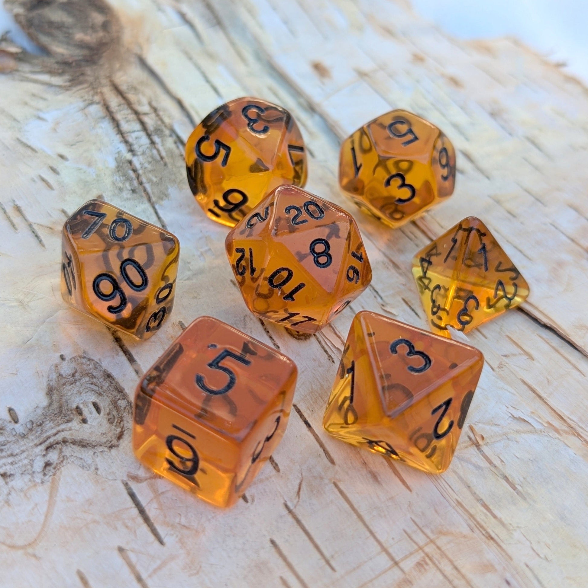 Amber Gems Dice Set with clear auburn hue on wood background, seven-piece TTRPG acrylic dice with black numbers