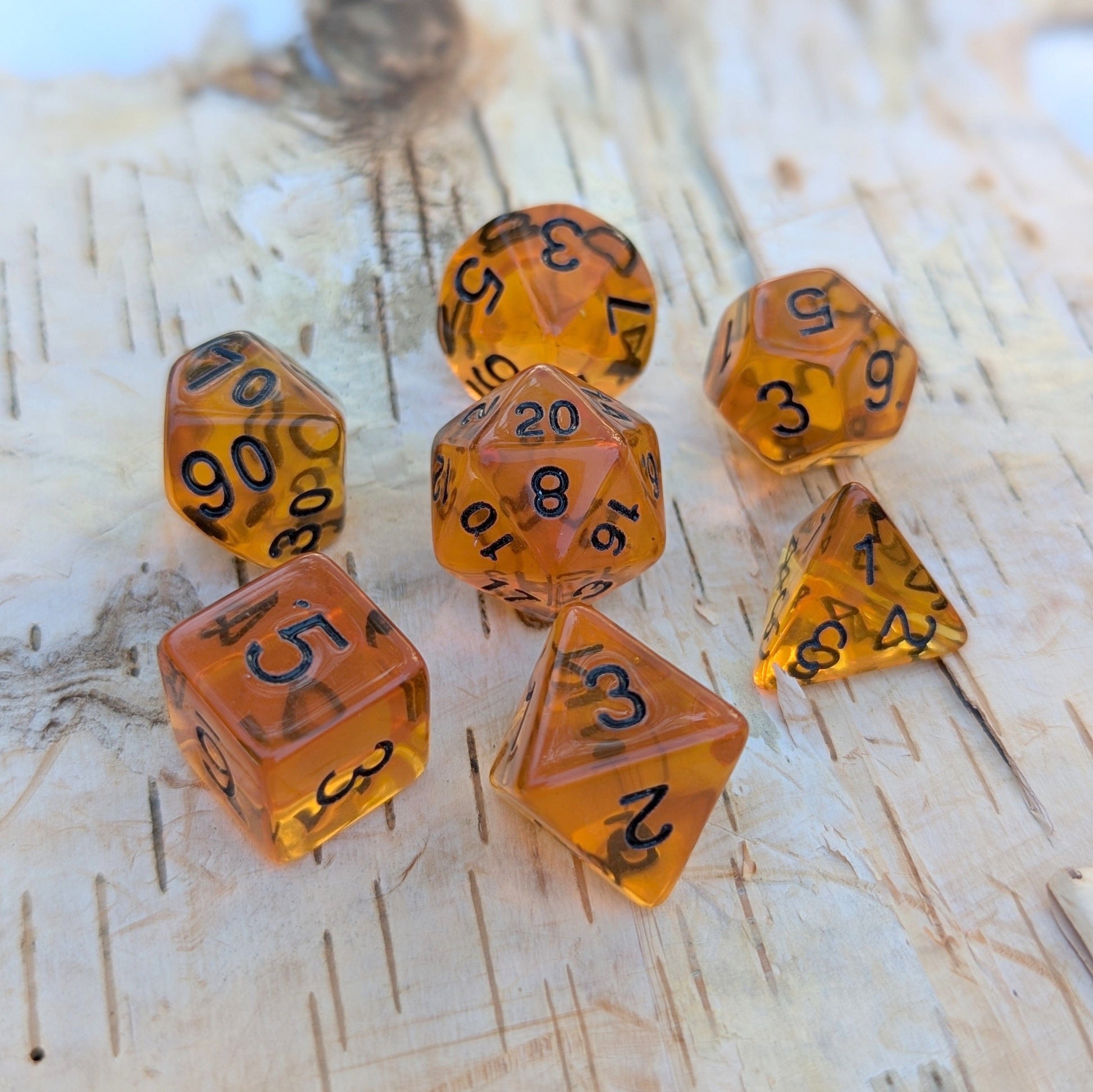 Amber Gems Dice Set with clear brown hue and black numbers for TTRPG like Dungeons & Dragons on wooden surface